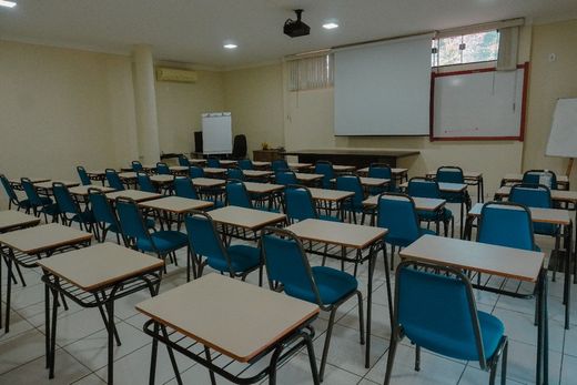 Uma sala de aula vazia com cadeiras e mesas azuis e uma tela de projetor.