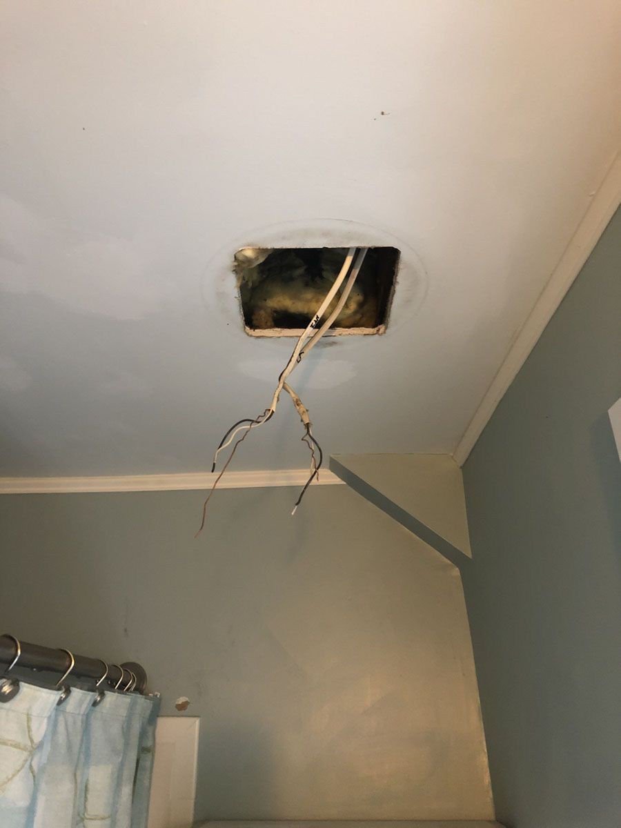 Hole in bathroom ceiling with exposed wires hanging down.