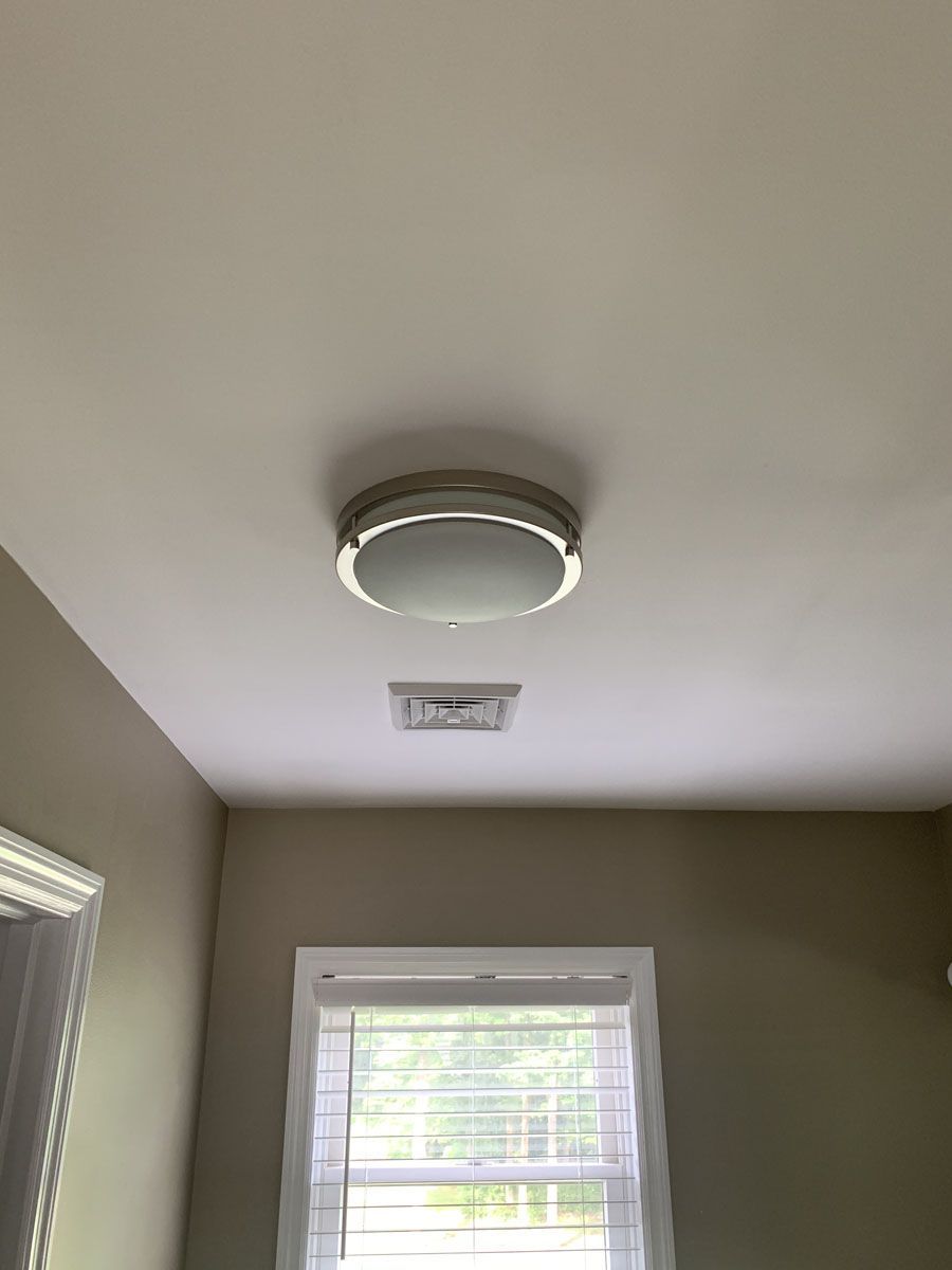 Ceiling light and vent above a window in a room with beige walls.