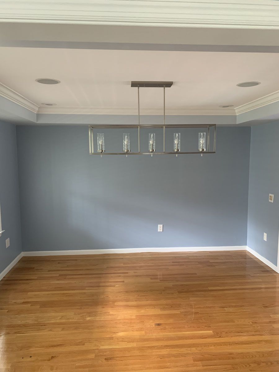 Empty dining room with blue walls, wood floor, white ceiling, and a modern chandelier.