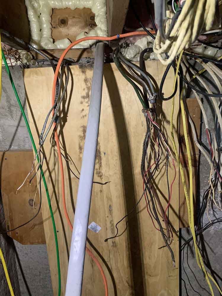 Exposed electrical wiring in a wood-paneled attic, with various colored wires and a conduit.