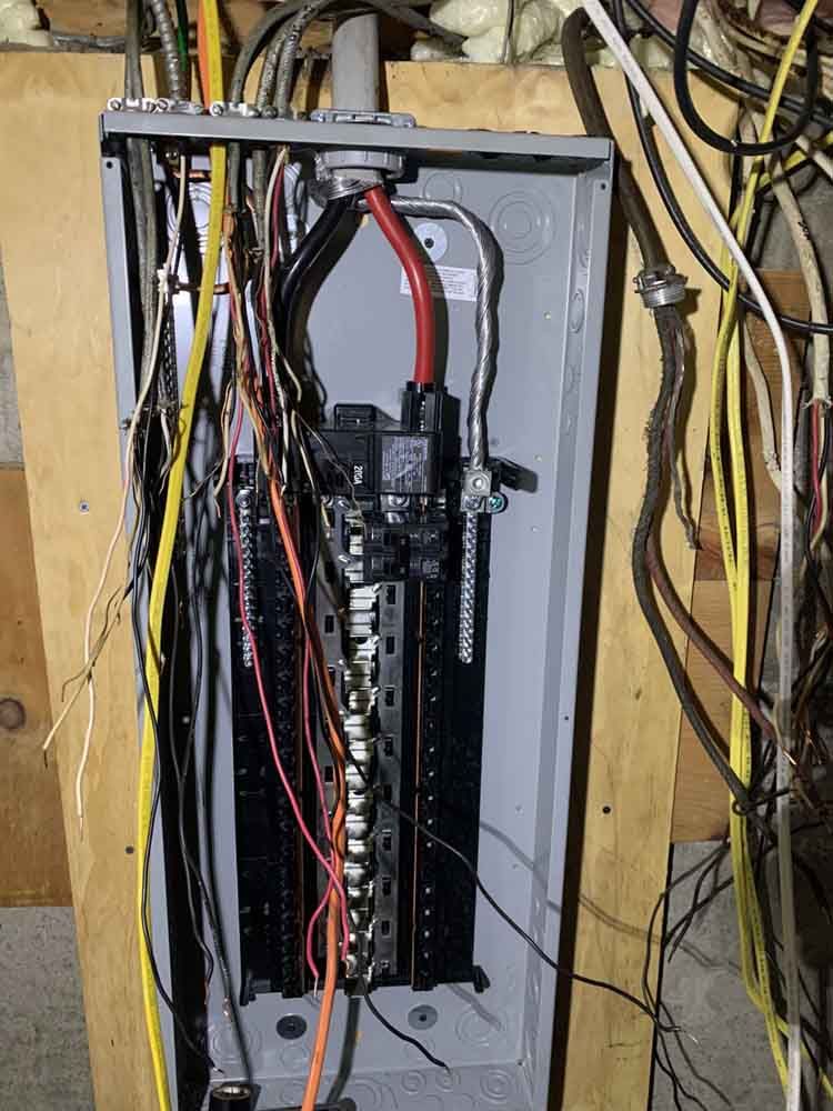 Electrical panel with numerous wires; mostly black, yellow, white, and gray. Inside a wall cavity.