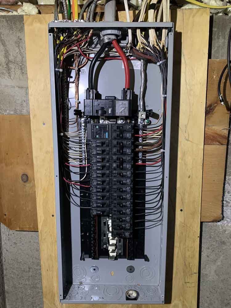 Electrical panel with numerous wires and circuit breakers, mounted on wooden supports.