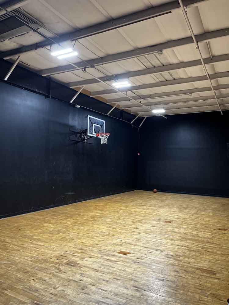 Basketball court with black walls, wood floor, and a hoop.
