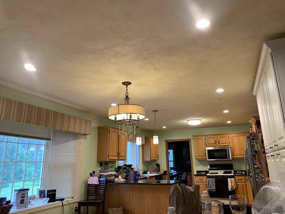 Kitchen with light-colored cabinets, recessed lighting, and a chandelier. Features a black countertop and window with view.