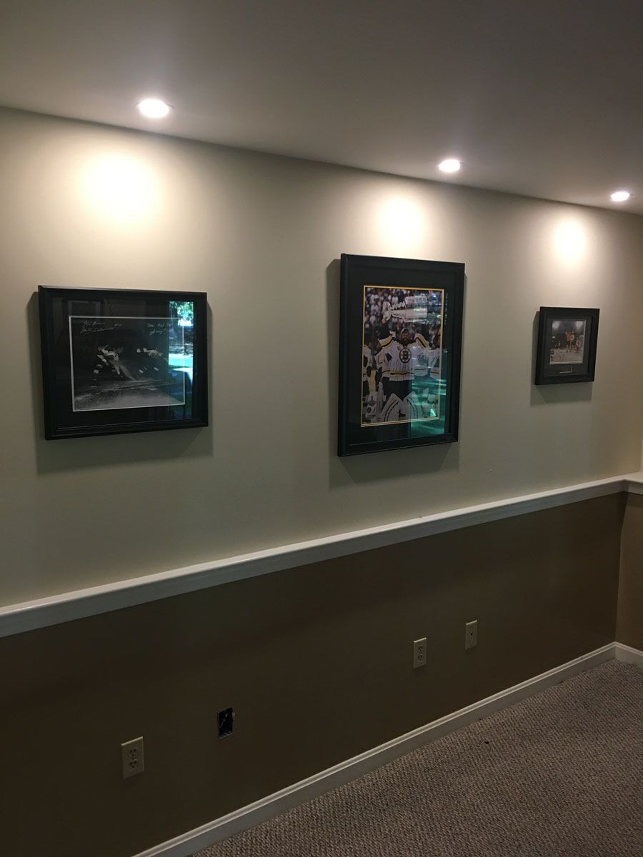 Three framed photos on a tan wall, lit by recessed ceiling lights. The wall has a darker tan lower section.