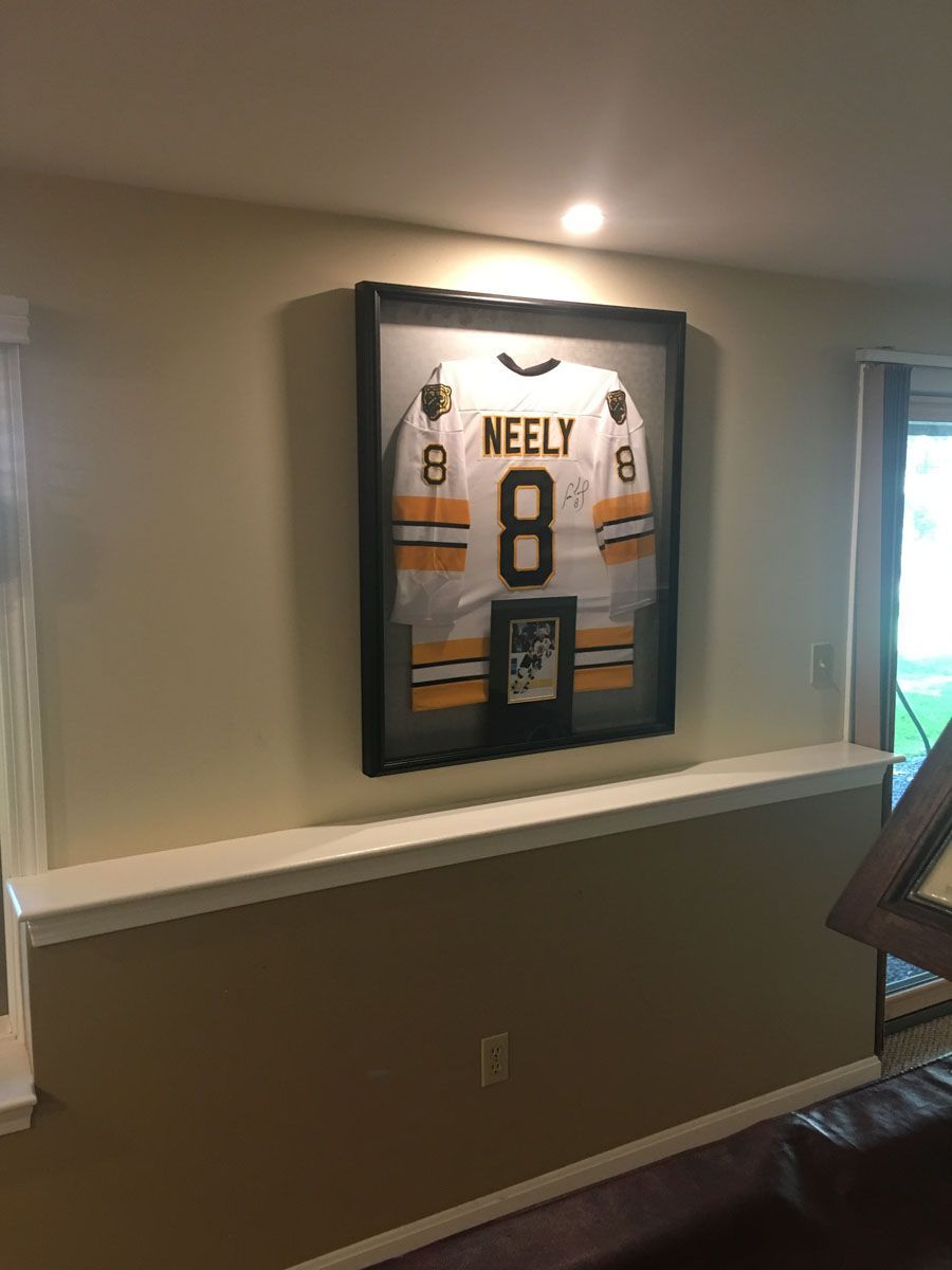 Framed hockey jersey of Neely (#8) on a wall, in a room with a ledge.