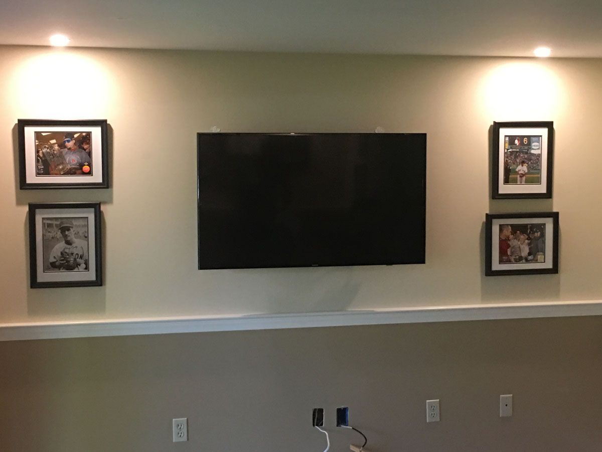 TV mounted on beige wall with framed photos and spotlights.