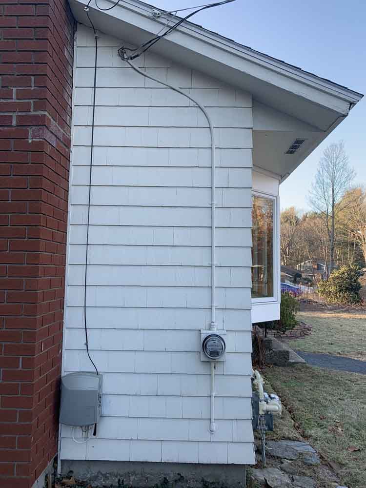 White siding of a house with electrical wiring and a meter; a brick chimney is to the left.