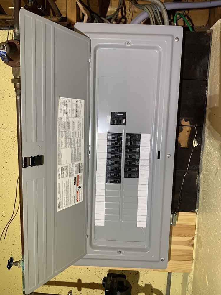 Electrical panel with door open, revealing circuit breakers. Gray metal box mounted on wood.