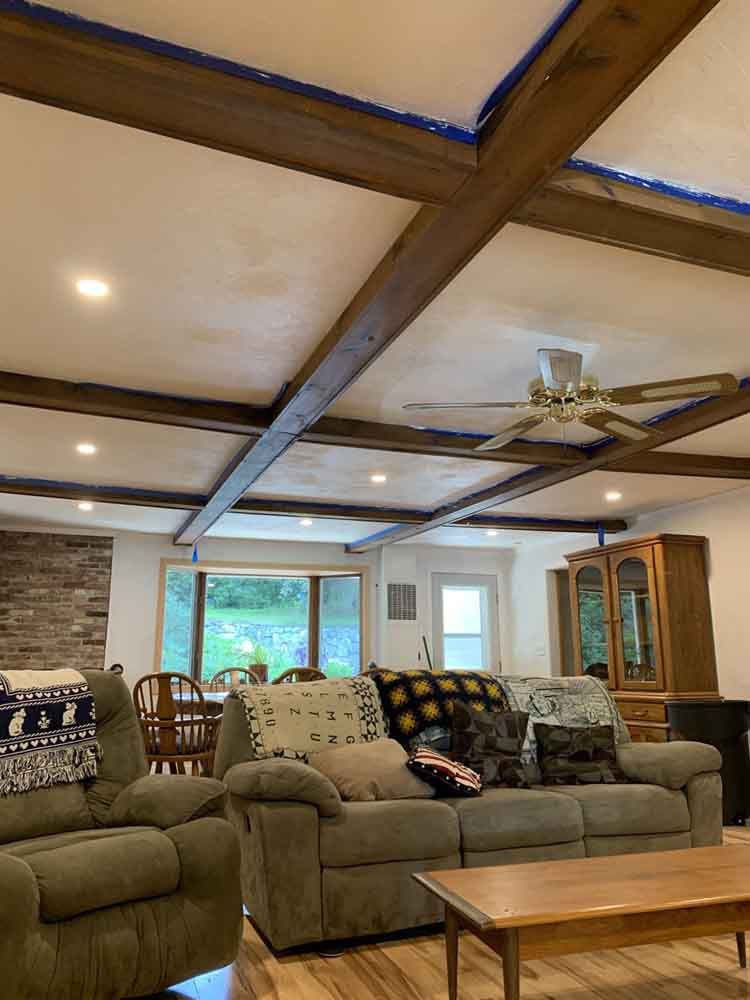 Living room with brown ceiling beams, recessed lights, and a green recliner and sofa.