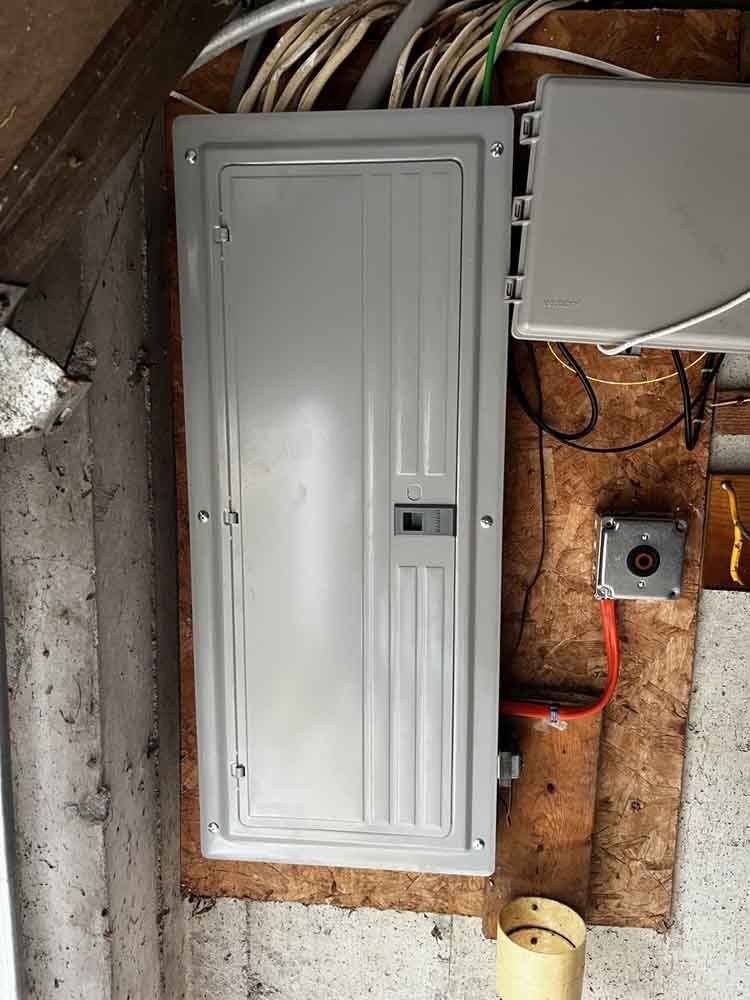 Electrical panel and related components mounted on wood paneling. Wires and conduits visible.