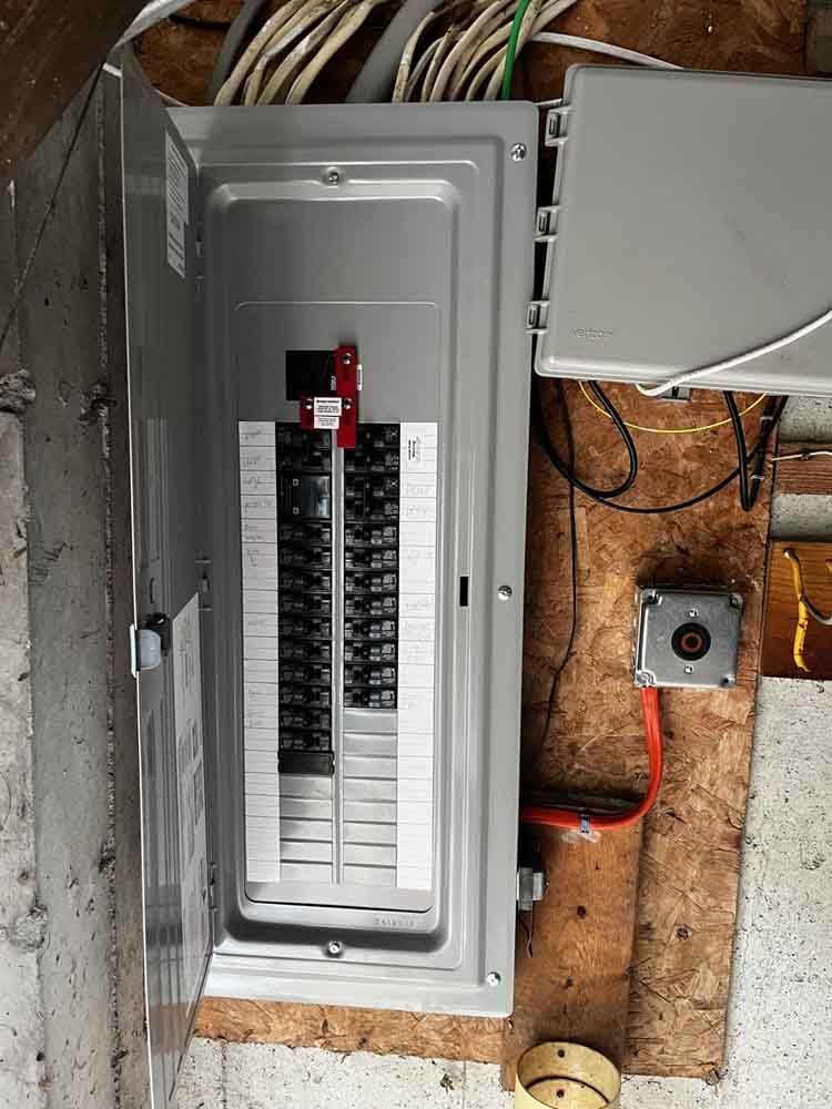 Open electrical panel with circuit breakers, wiring, and conduit in a wooden structure.
