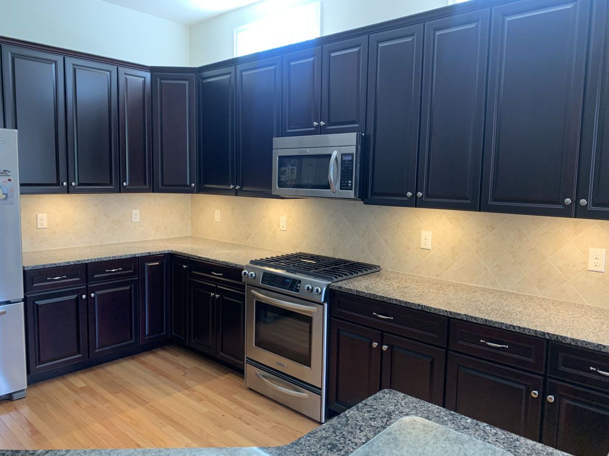 Dark kitchen cabinets with stainless steel appliances, light countertops and hardwood floors.