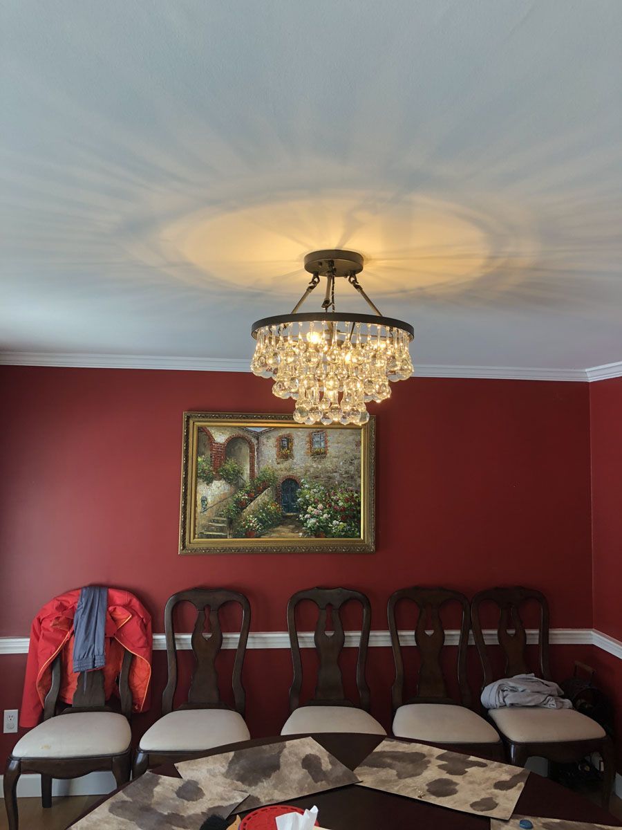 Dining room with chandelier, red walls, framed art, wooden chairs, table runner, and a jacket on a chair.