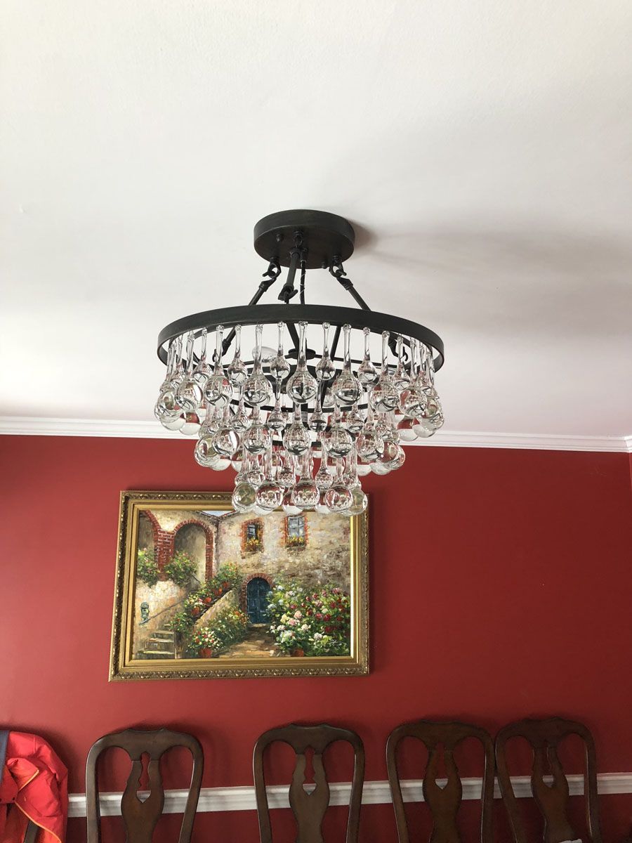 Crystal chandelier hanging above a framed painting and wooden dining chairs against a red wall.