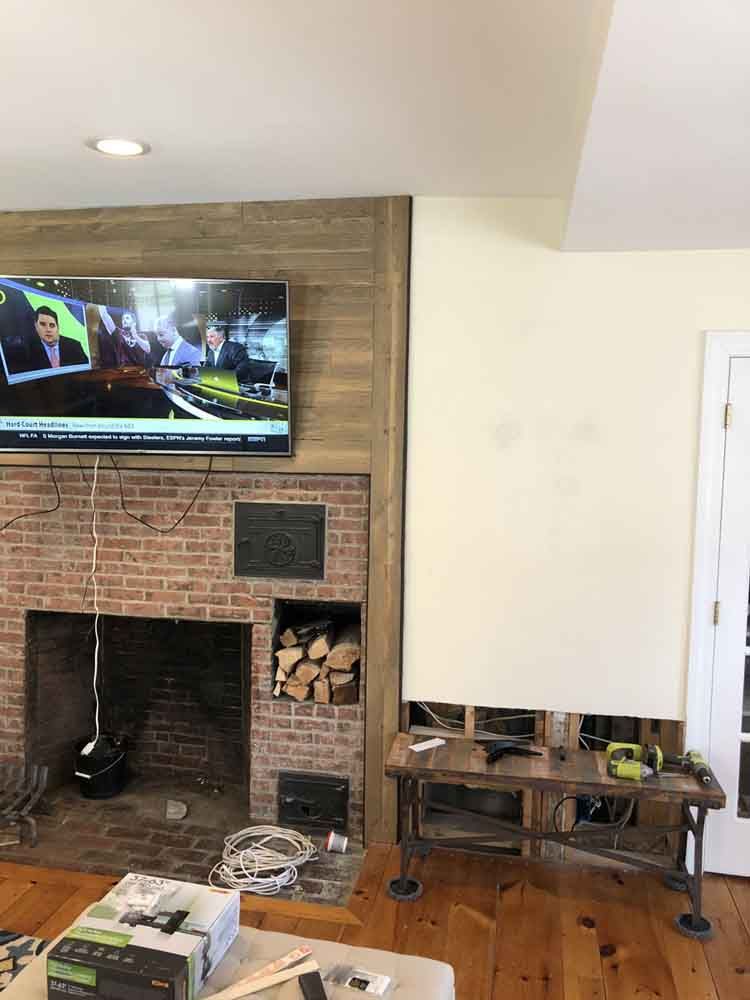 Living room with a brick fireplace and TV; a wooden desk sits against a cream wall.