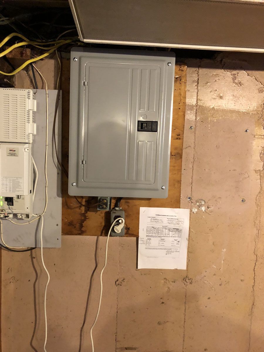 Electrical panel and related wiring mounted on a painted wooden wall, with a small diagram posted nearby.