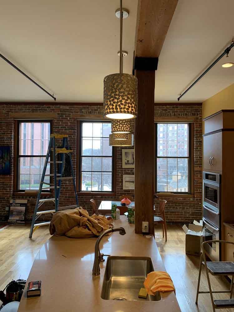 Kitchen with island, exposed brick, pendant lights, windows, wooden beam, and hardwood floor.
