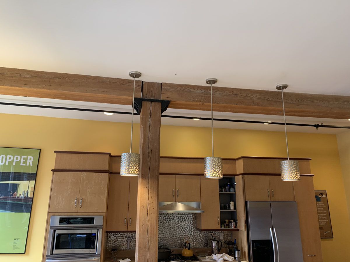 Kitchen with wooden support beams, pendant lights, cabinets, and appliances.