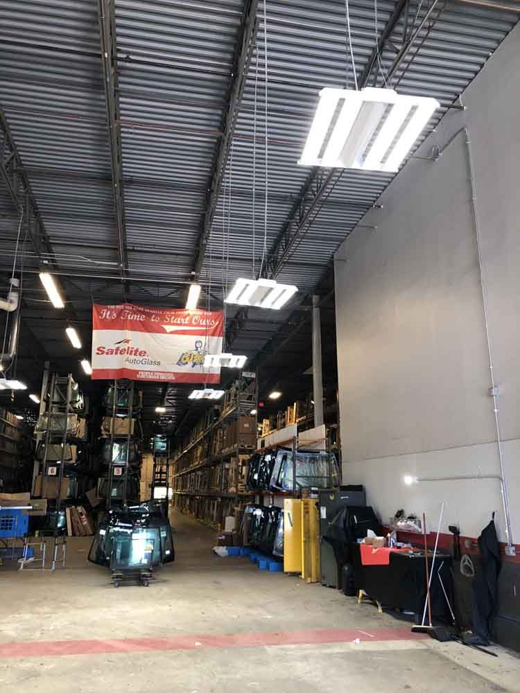 Warehouse interior with rows of shelves stocked with parts and a hanging sign. Fluorescent lighting from the ceiling.