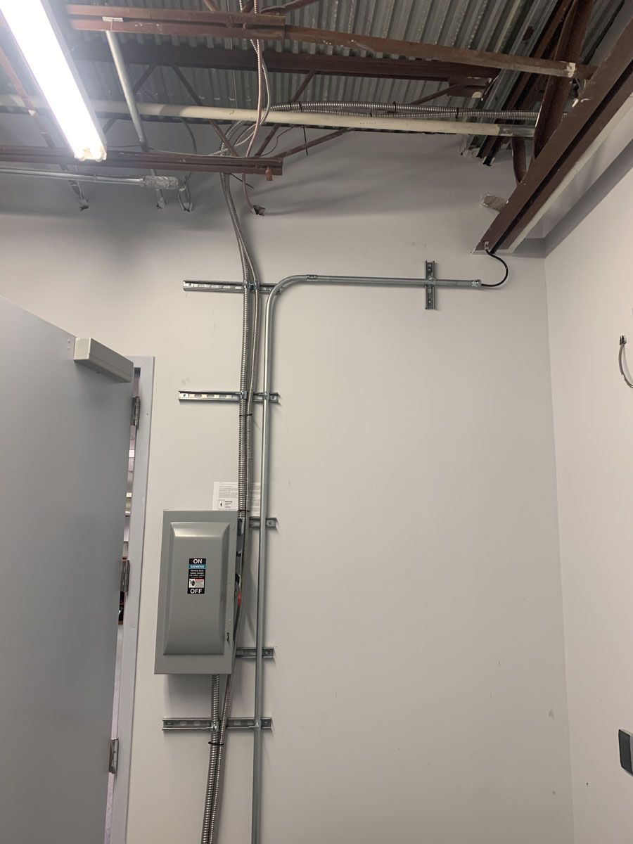 Electrical conduit and control box mounted on a white wall, running to ceiling with metal beams.