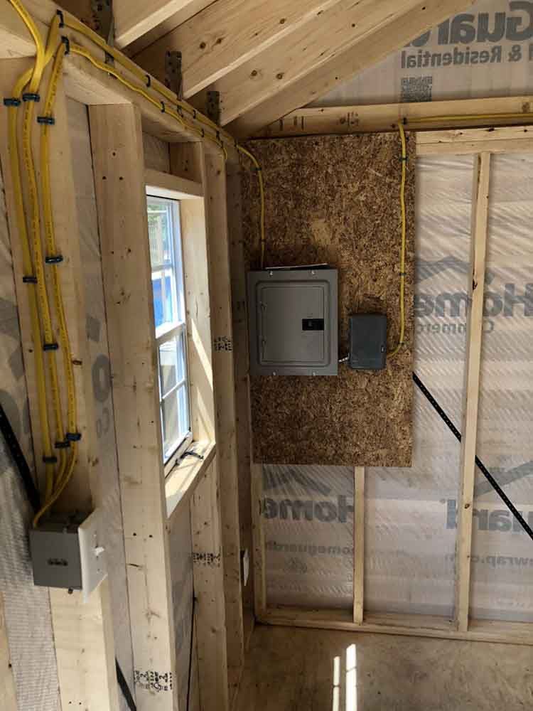 Interior of a wooden structure showing electrical wiring and a breaker box mounted on a wall.