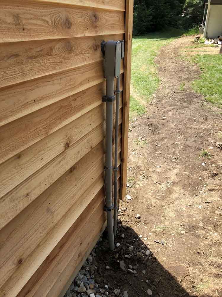 Gray electrical conduit on a wooden building's exterior, extending vertically along the wall.