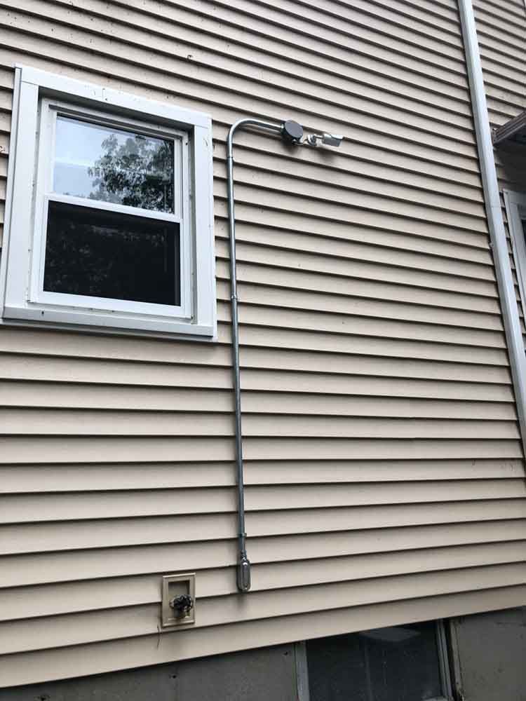 Tan siding with a window, metal conduit, and electrical box on a house exterior.