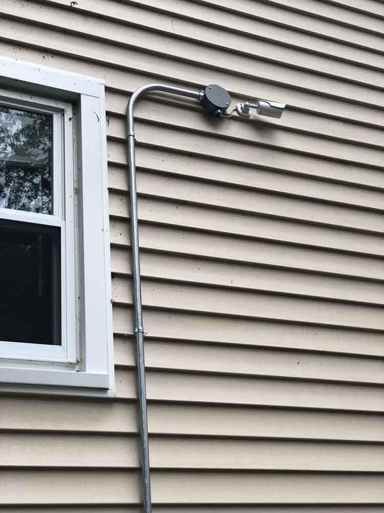 Exterior view: metal conduit and light fixture on beige siding near a window.