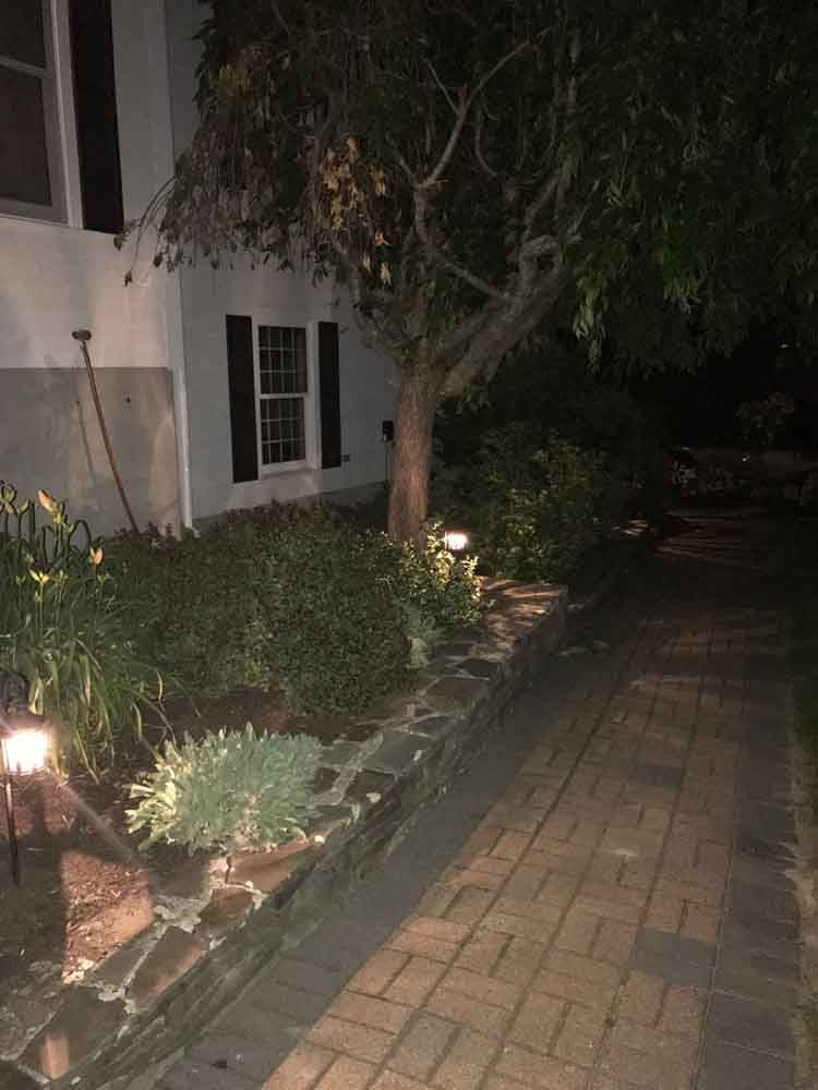 Nighttime view of a house with a brick pathway, landscaping, and lit by path lights.