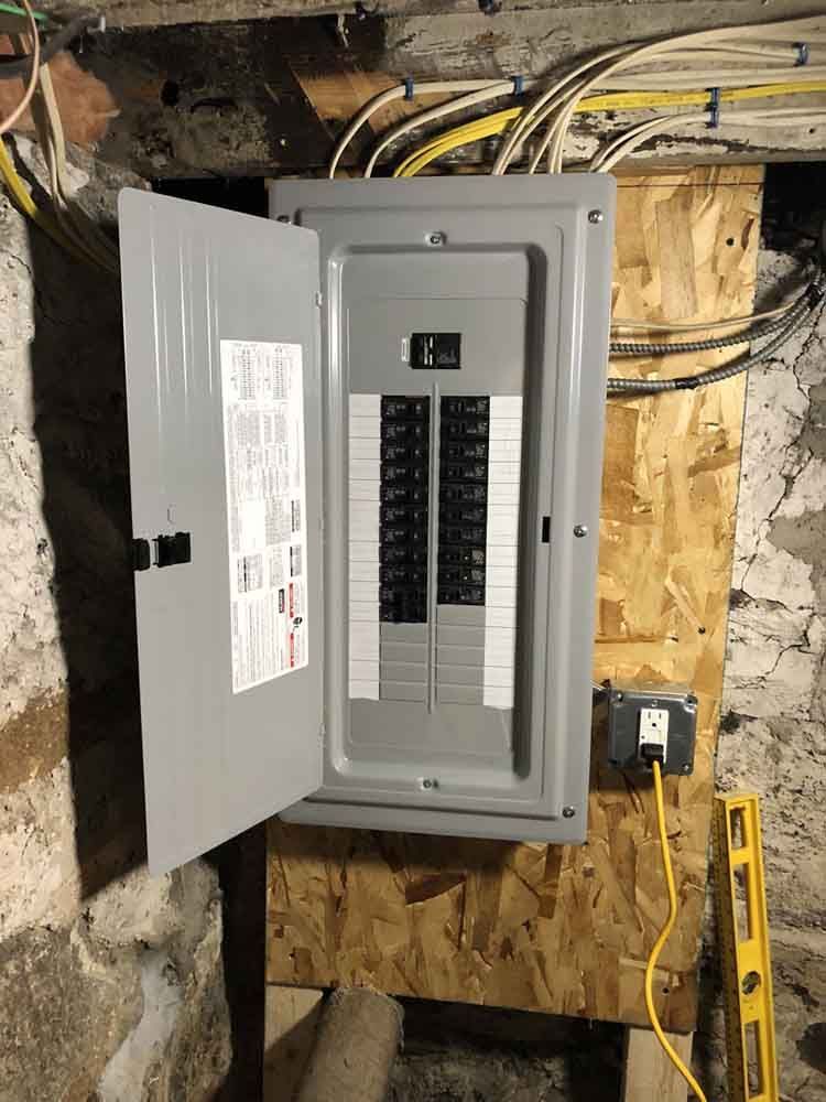Electrical panel with open door, mounted on wood, with wires and electrical outlet nearby.