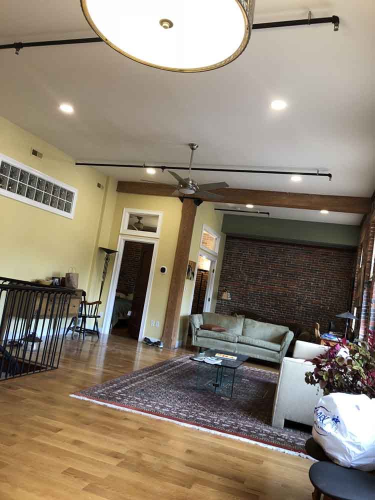 Spacious living room with light wood floors, beige couch, and exposed brick wall.