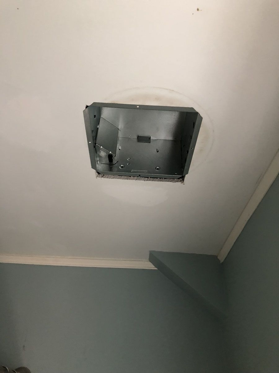 A metal vent frame is exposed on a white ceiling, likely for a fan or light. Pale blue wall below.
