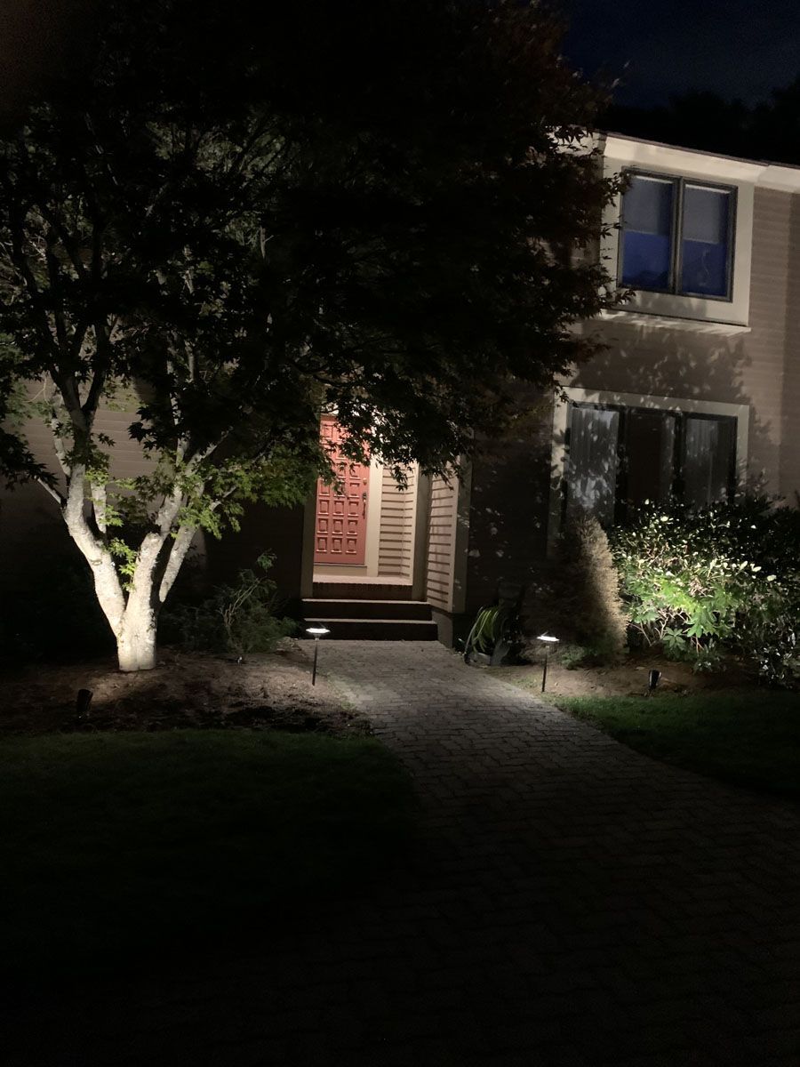 Nighttime view of a house with illuminated landscaping and pathway leading to the front door.