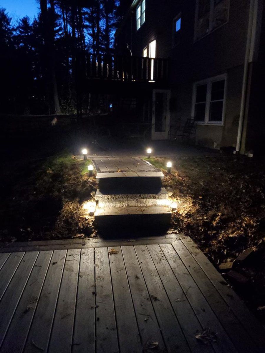 Wooden steps and pathway illuminated by lights leading to a house at night.