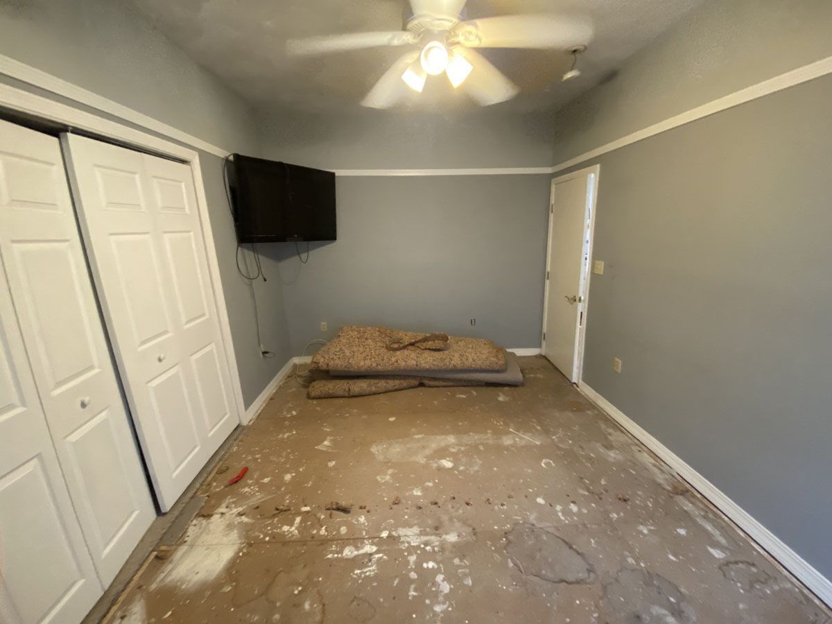 Empty room with grey walls, white trim and doors, and damaged flooring.