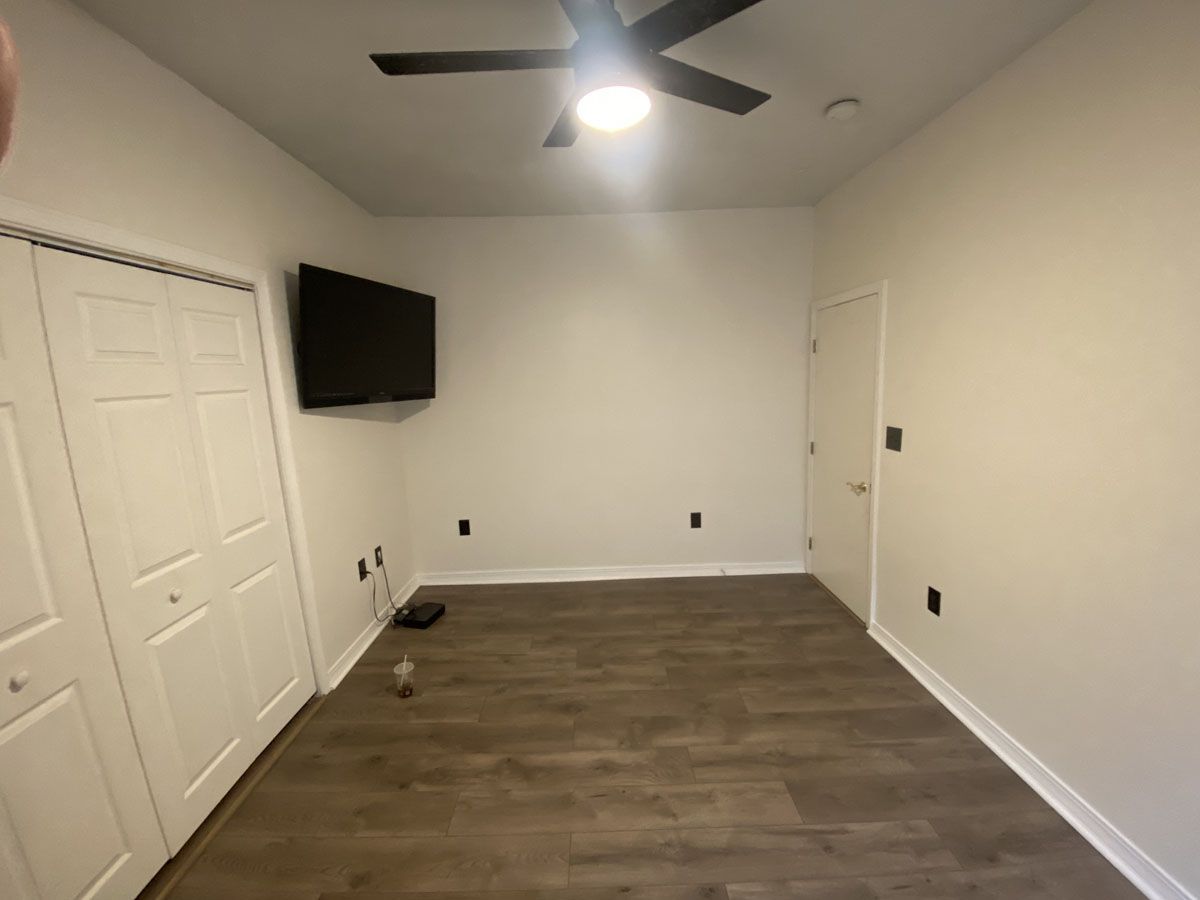 Empty room with wood-look floor, white walls, closet, TV, door, and ceiling fan.