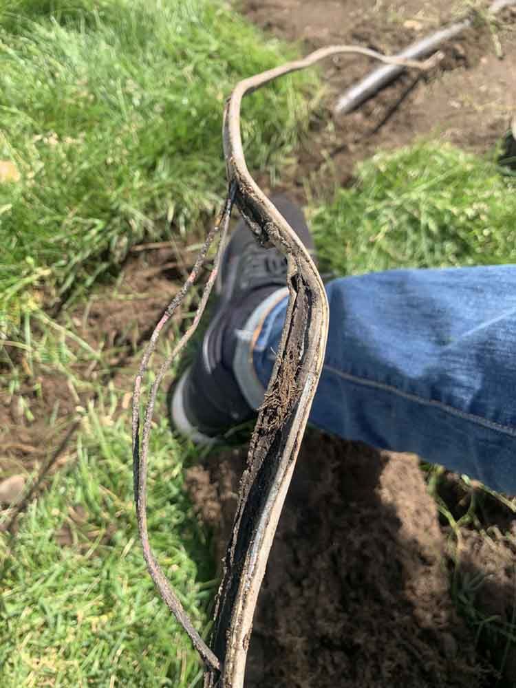 A person's foot and jeans next to a damaged black cable on grass and dirt, outdoors.