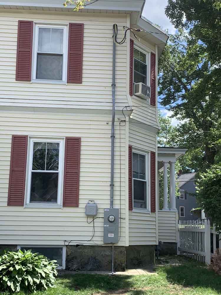 Two-story house with cream siding, red shutters, and electrical conduit running up the side.