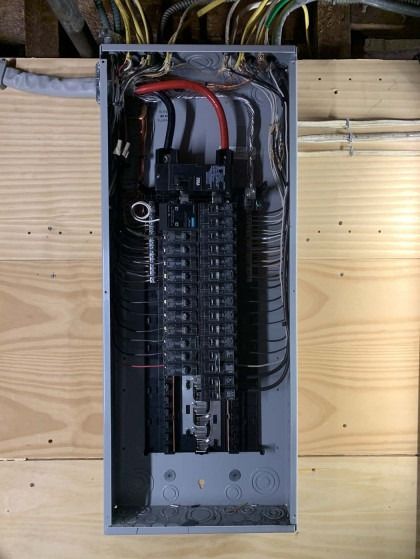 Open electrical panel with black circuit breakers, red and black wires, and various colored wires at top.