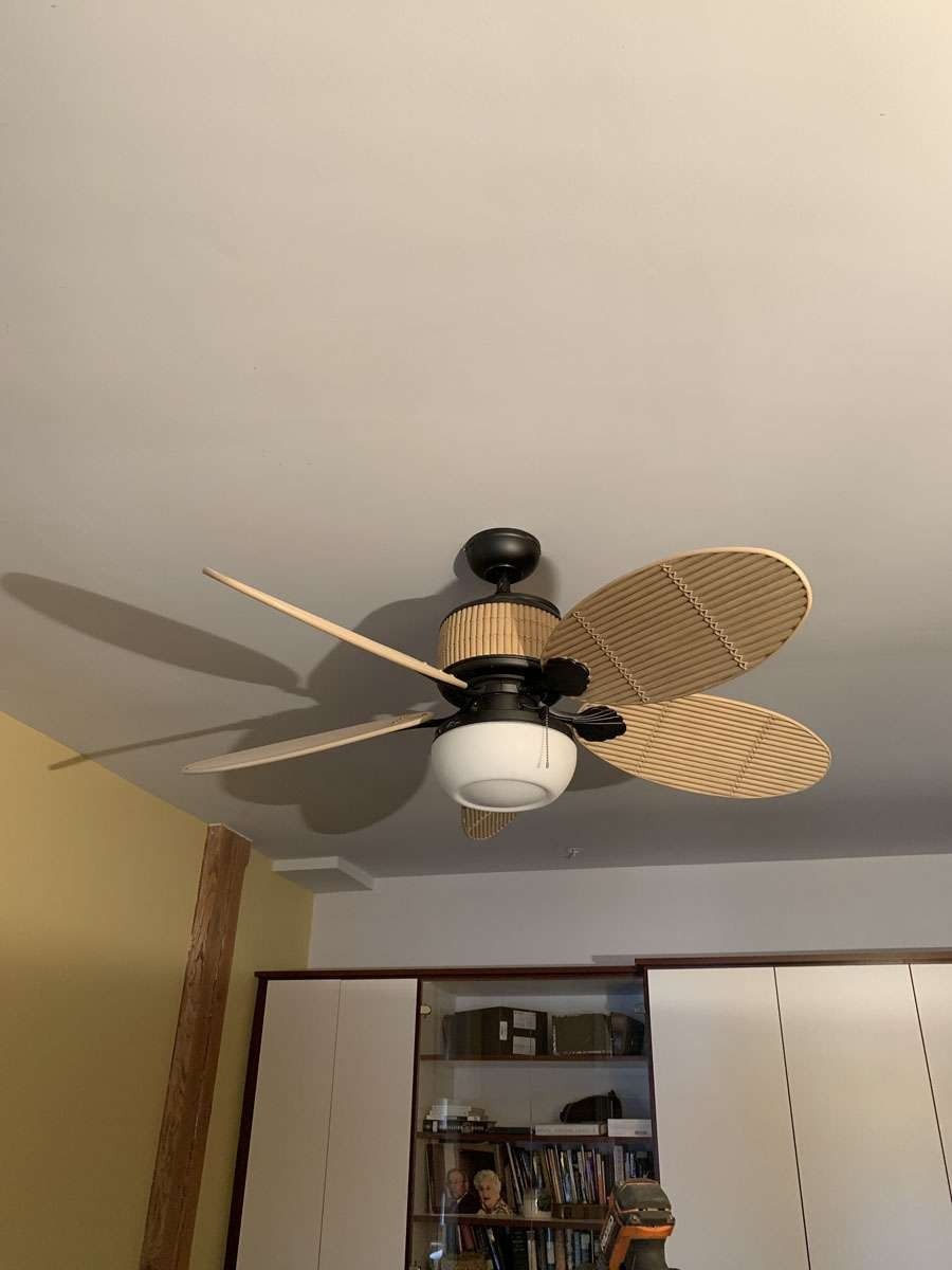 Ceiling fan with beige and black accents; hanging in room with white walls and wood cabinets.