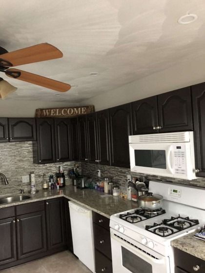 Dark brown kitchen cabinets and appliances, with a white microwave, and a ceiling fan.