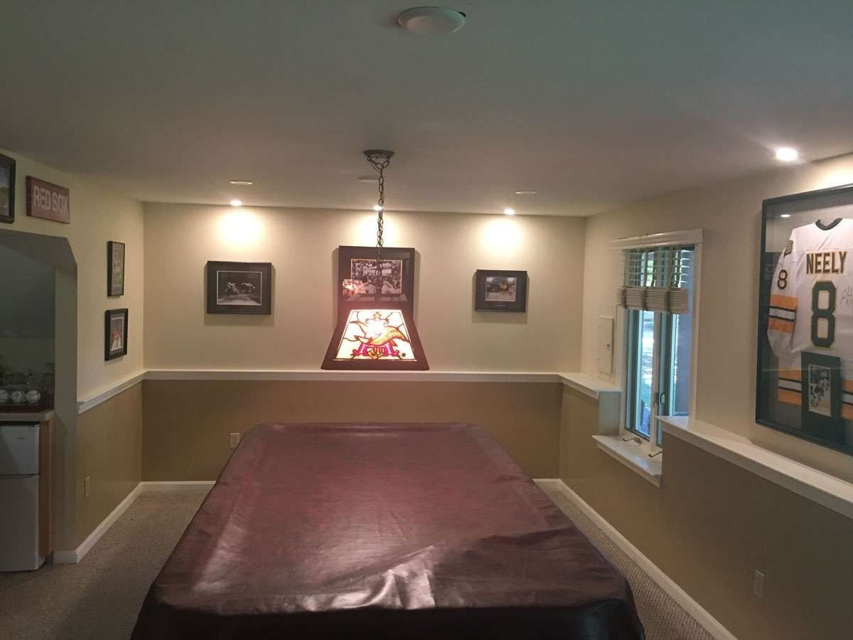 Pool table in a basement rec room, with a light fixture above. Beige and brown color scheme.