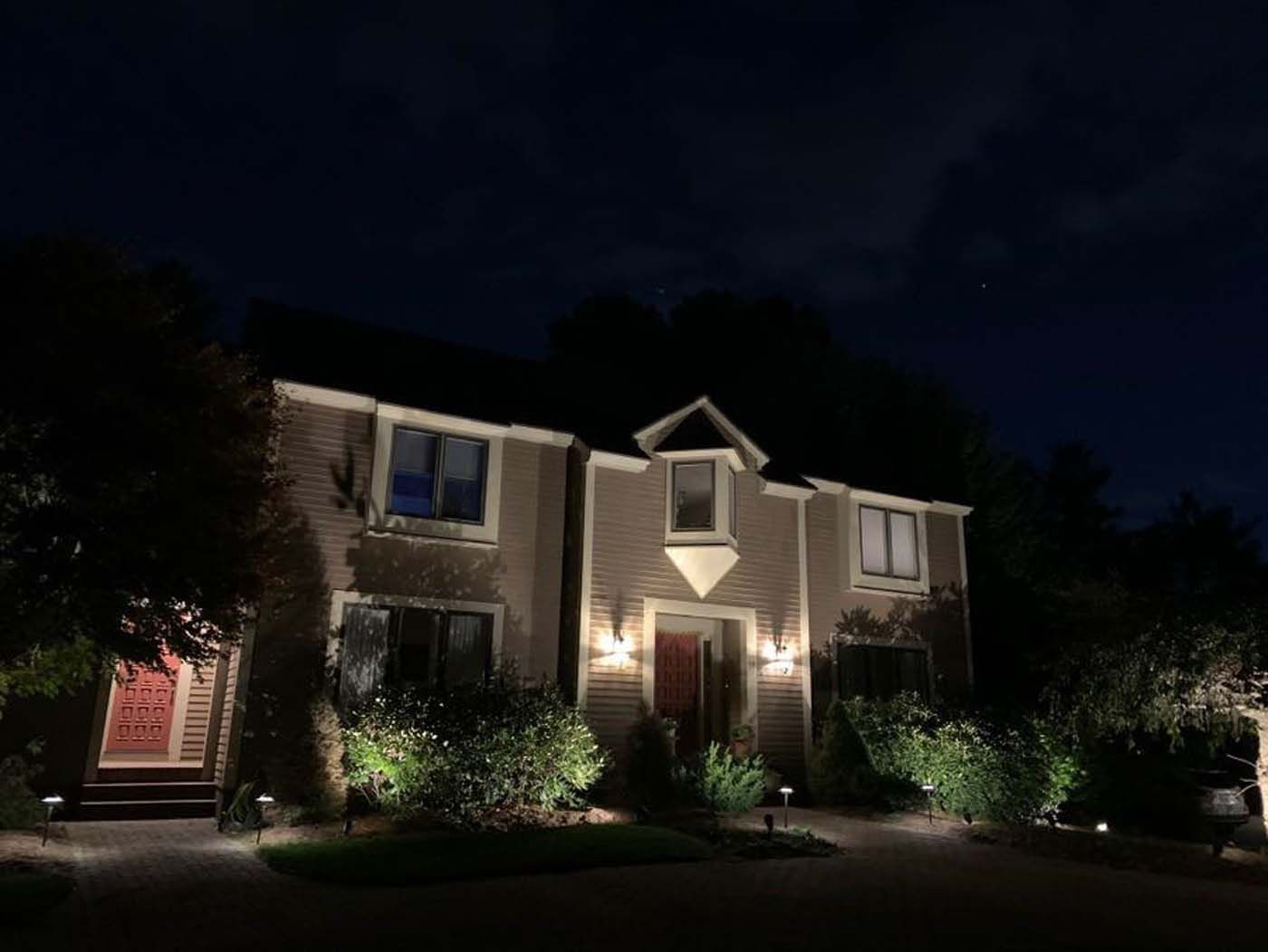 House at night with exterior lighting, shrubs, and two doors.