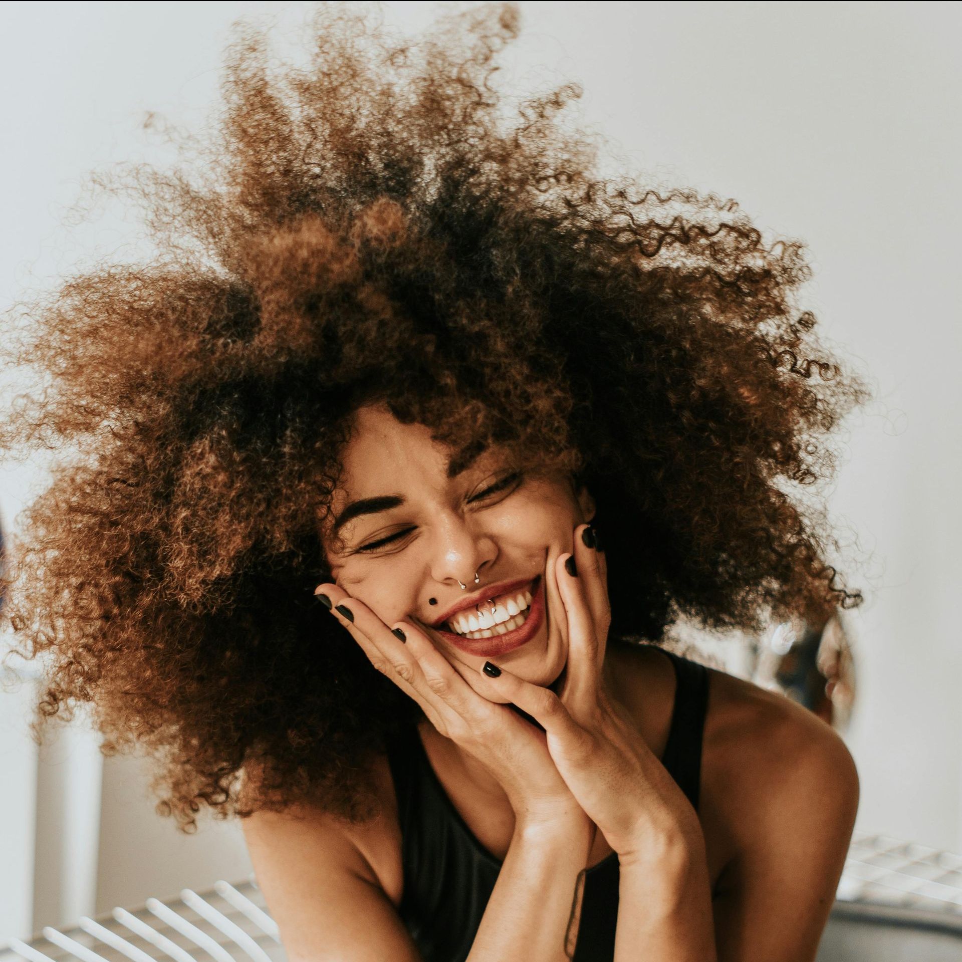 A woman with curly hair is smiling with her hands on her face