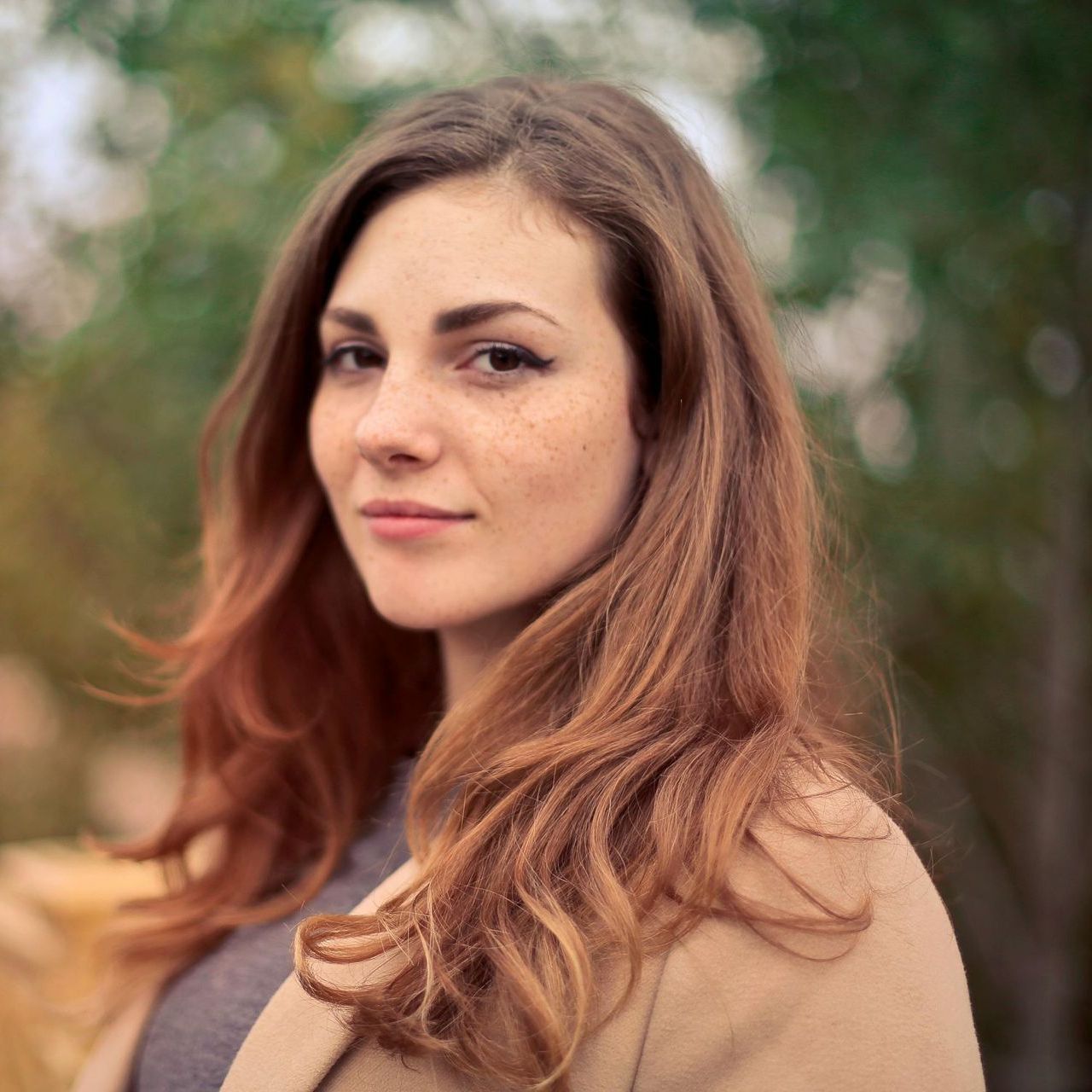 A woman with long red hair is wearing a tan coat