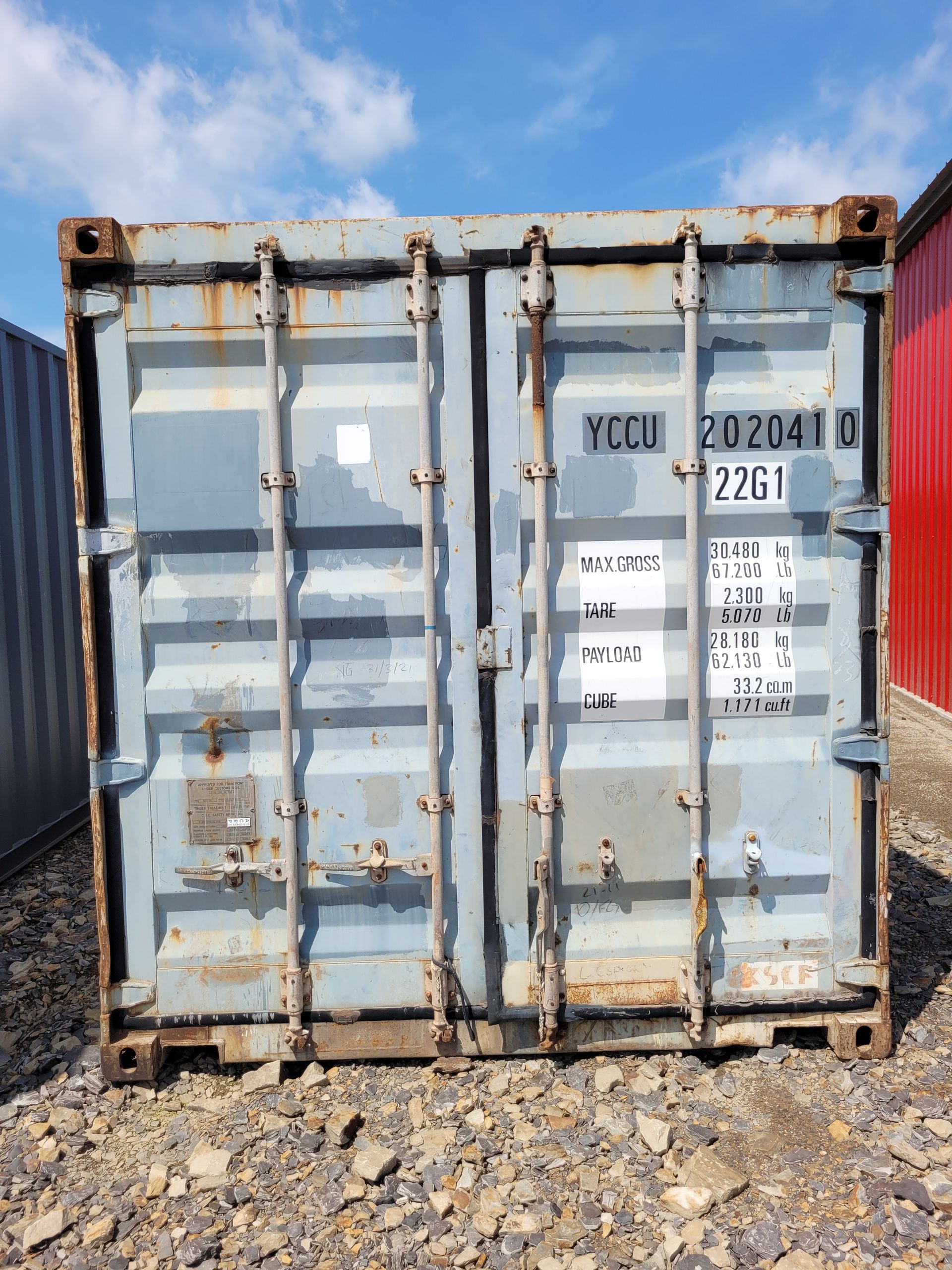 A shipping container is sitting on a gravel road.