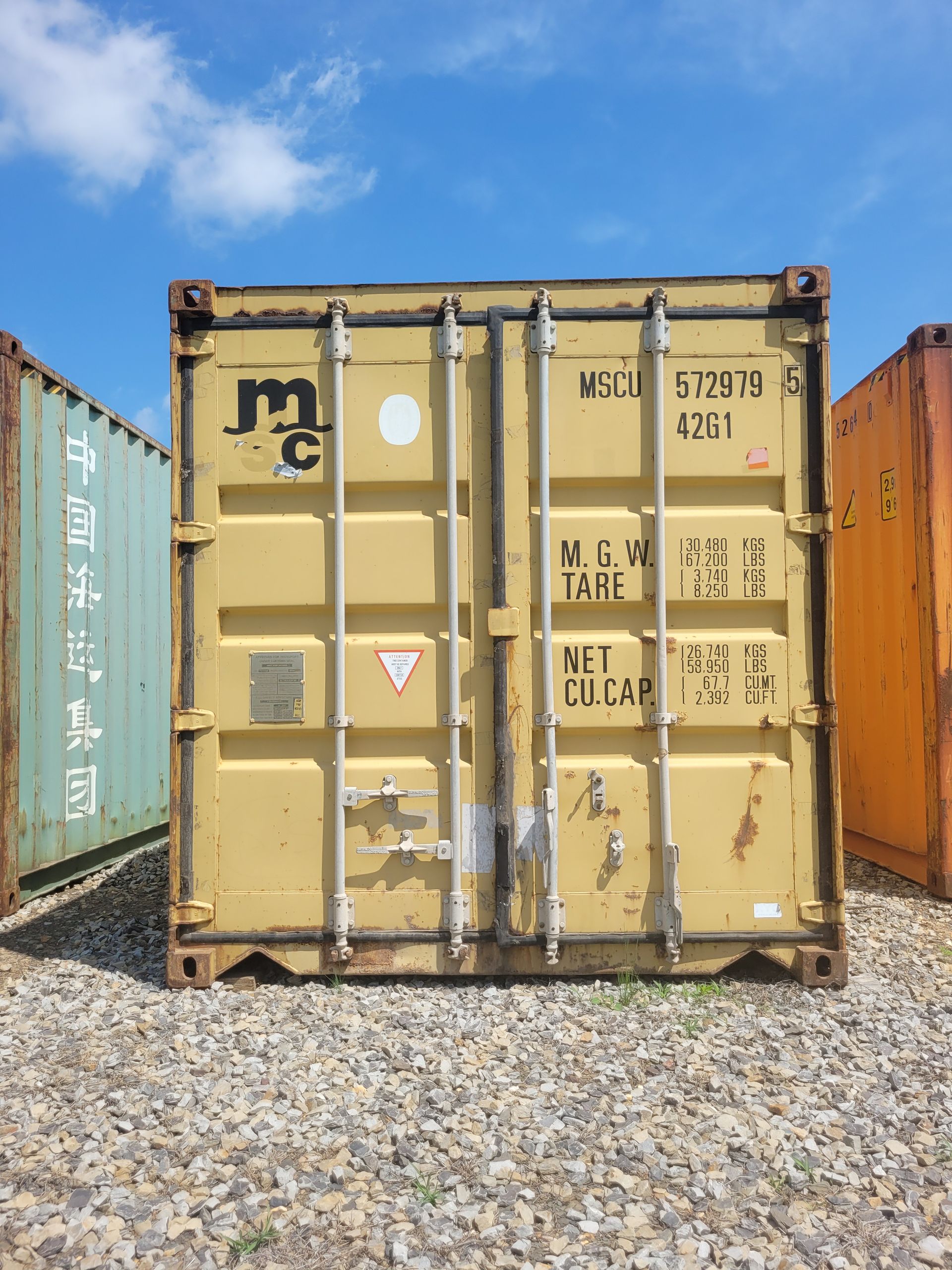 A yellow shipping container is sitting on top of a gravel lot.