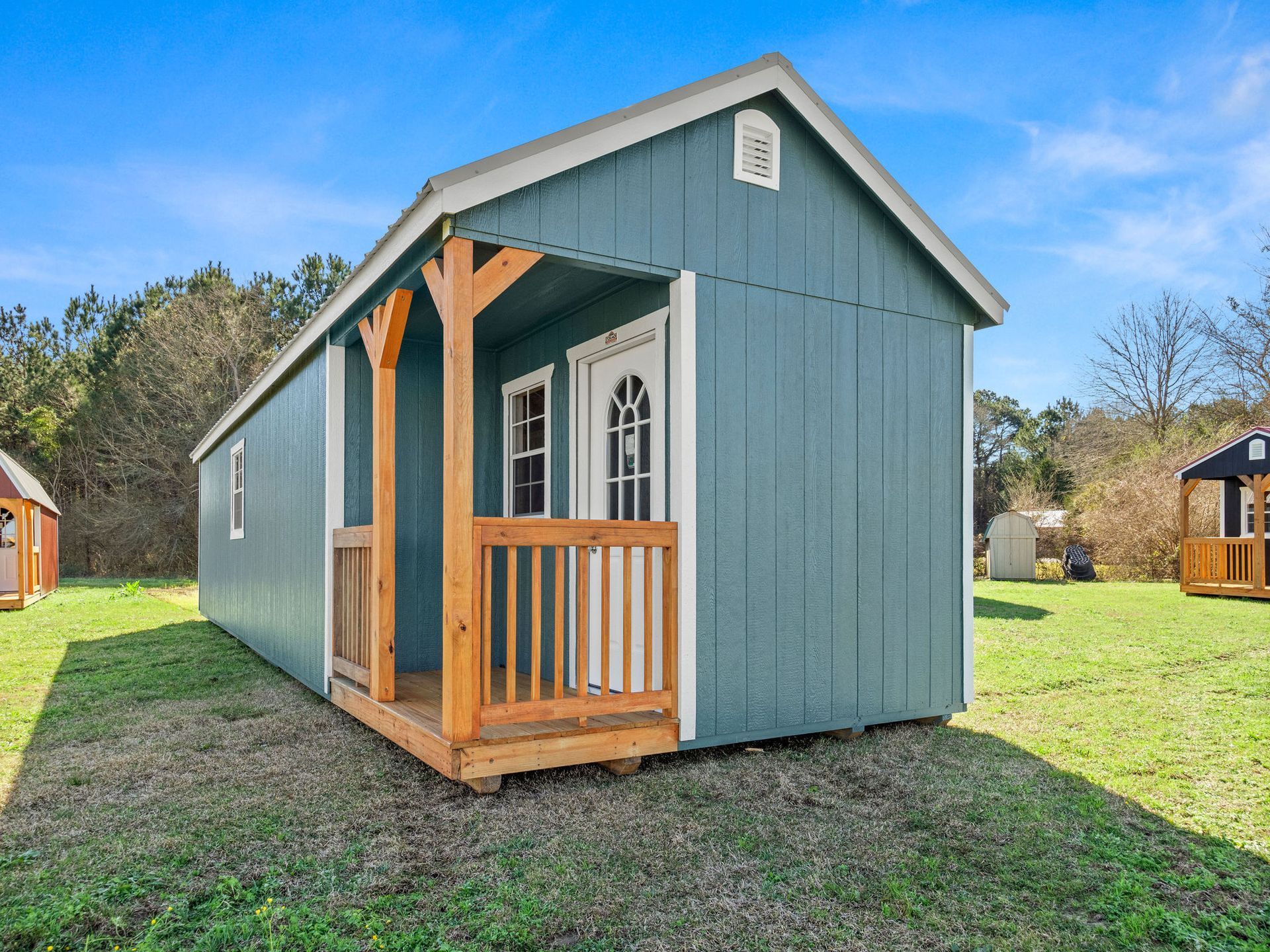 Superior Outdoor Centers deluxe side cabin A blue shed with a porch is sitting in the middle of a grassy field.